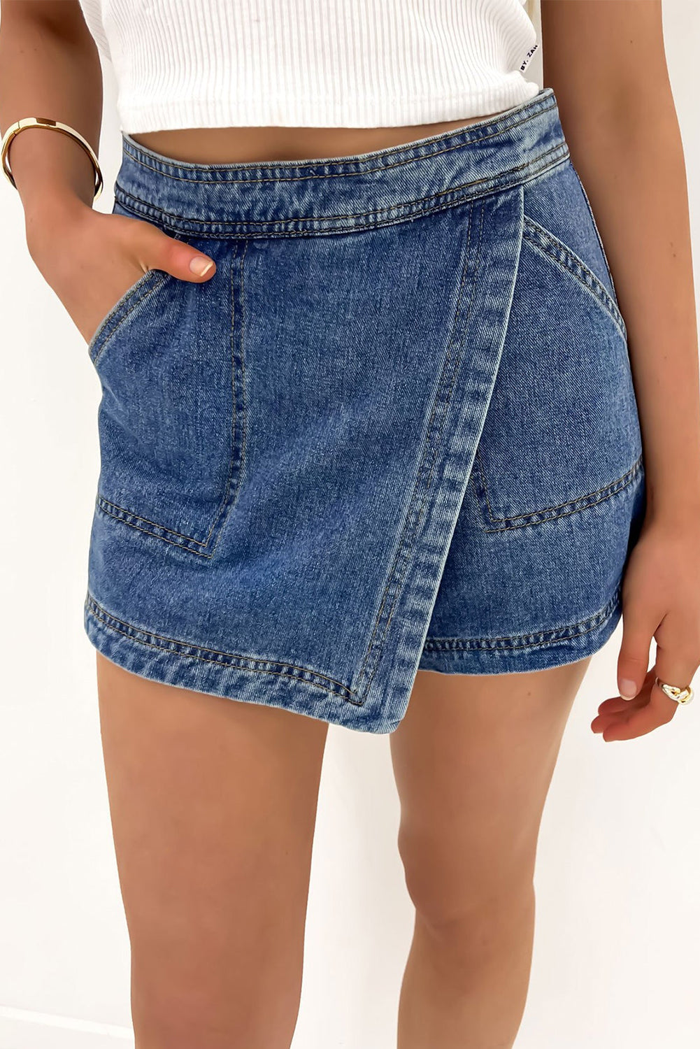Blue faux-wrapped denim mini skort with front patch pockets and crossover hem