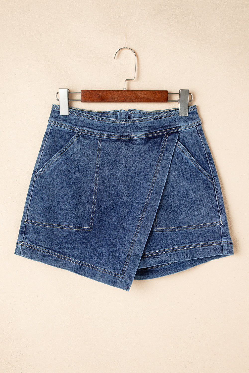Blue denim mini skort hanging on a hanger, faux-wrap design with pockets