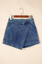 Blue denim mini skort hanging on a hanger, faux-wrap design with pockets