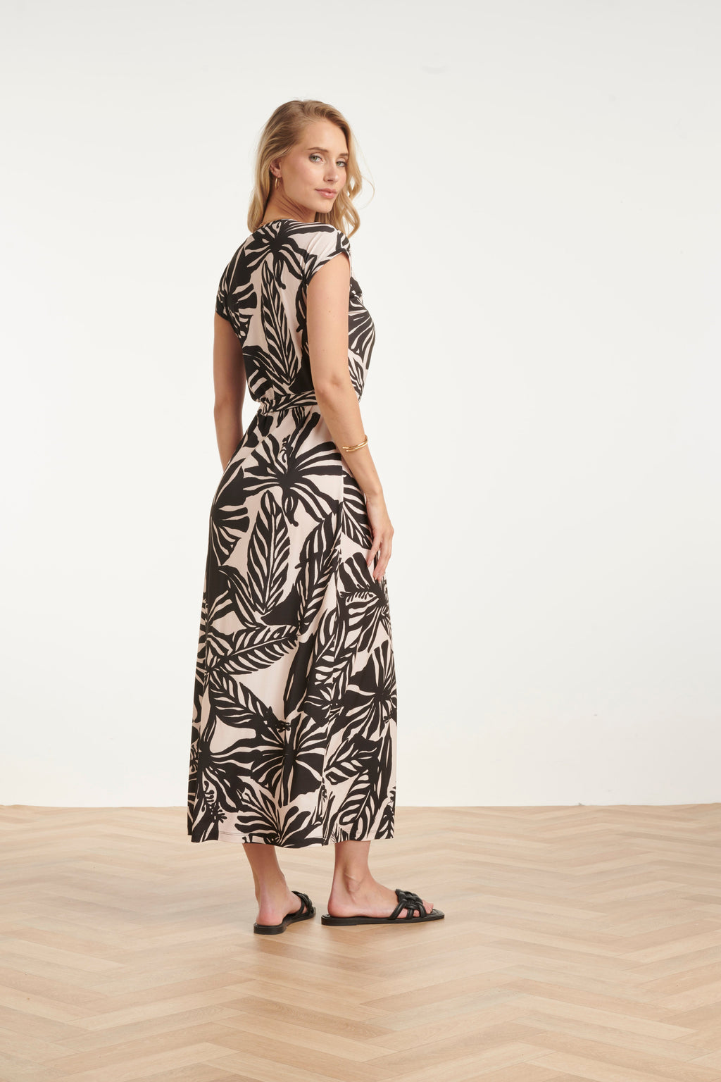 Women's black maxi dress with off-white leaf print, back view with gathered waist tie