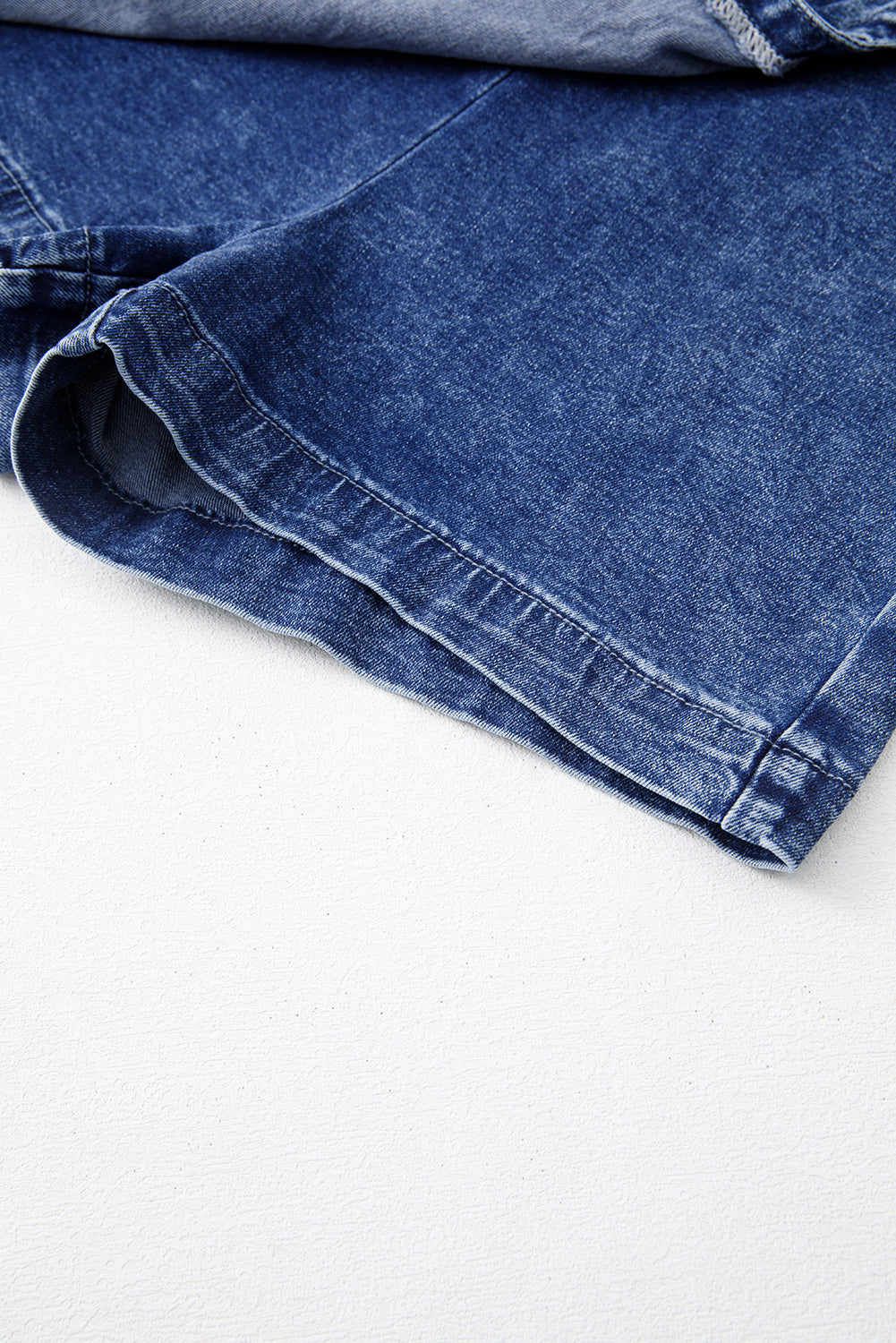 Blue acid-wash denim skort hem with visible seam stitching and folded edge
