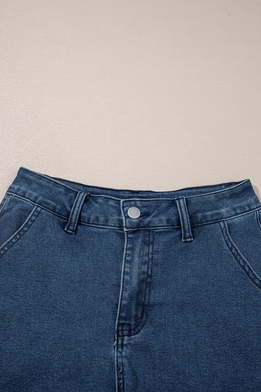 Close-up of high-waist blue denim shorts waistband with button closure and belt loops