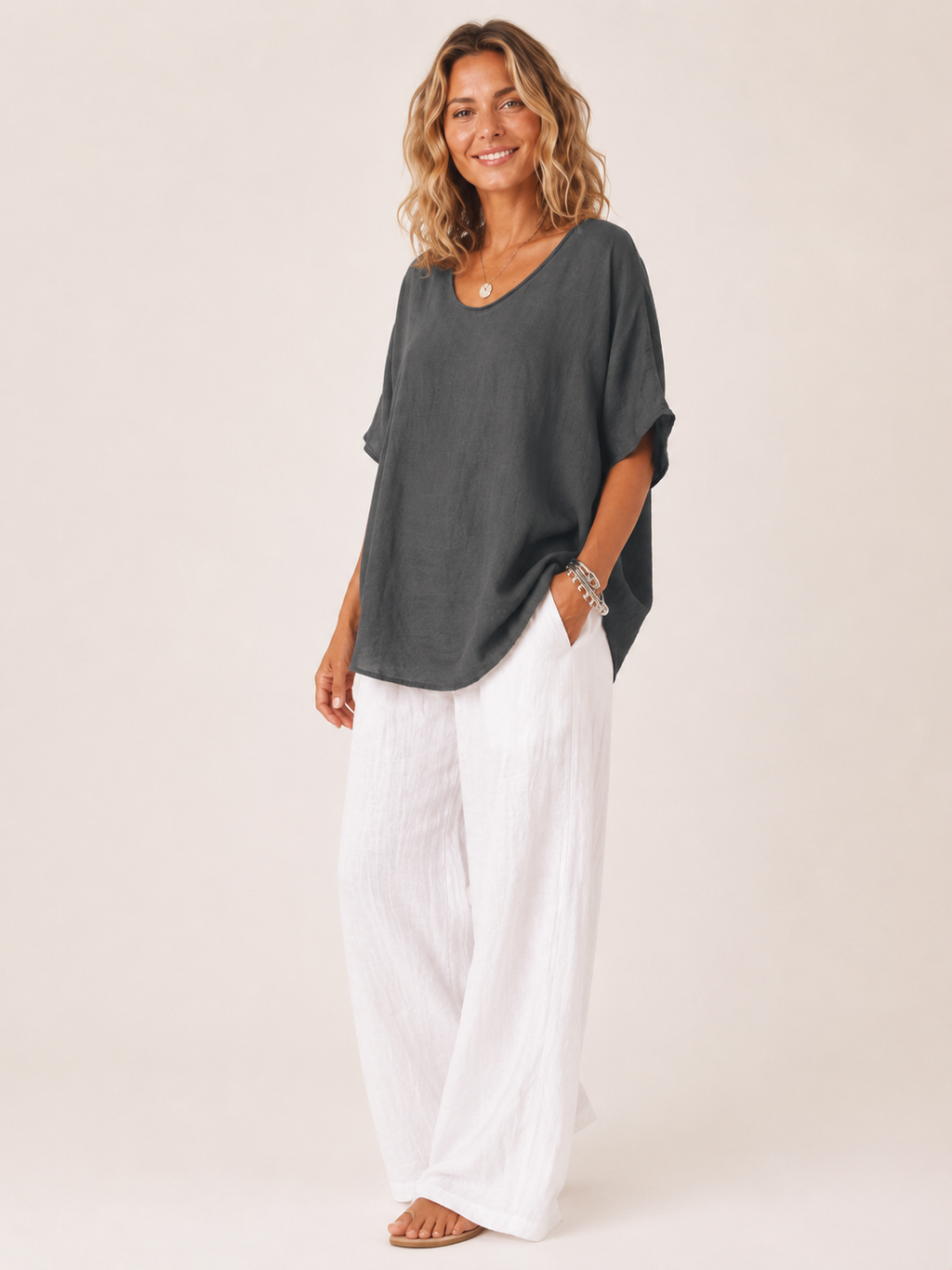 Women’s loose V-neck dark gray top with short wide sleeves, worn over white pants.