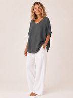 Women’s loose V-neck dark gray top with short wide sleeves, worn over white pants.