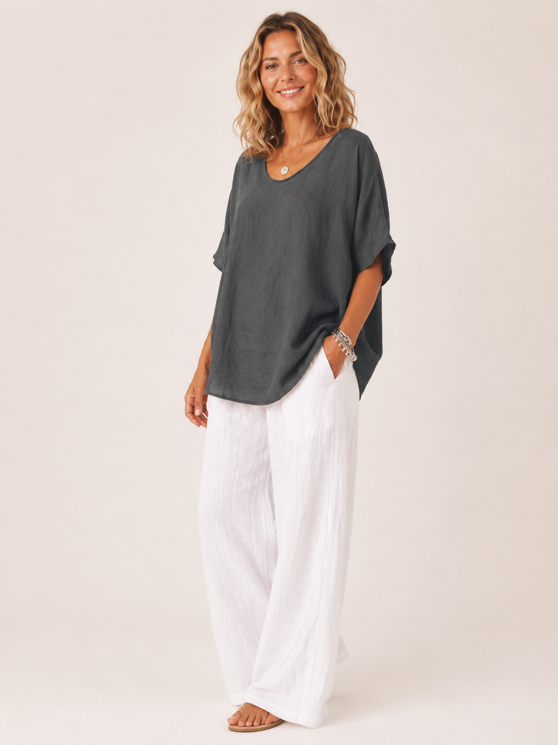 Women’s loose V-neck dark gray top with short wide sleeves, worn over white pants.