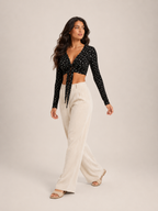 Black long-sleeve V-neck crop top with front tie and allover ditsy print, standing