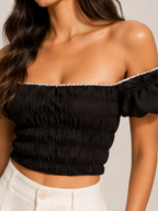 Black smocked off-shoulder top close-up with elastic ruffle edge and puff sleeve