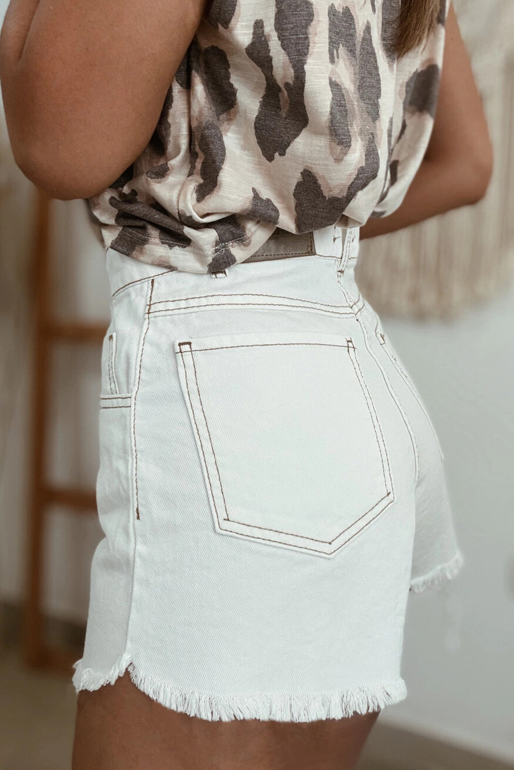 White high-waist denim shorts with frayed hem and back patch pocket; contrast stitch.