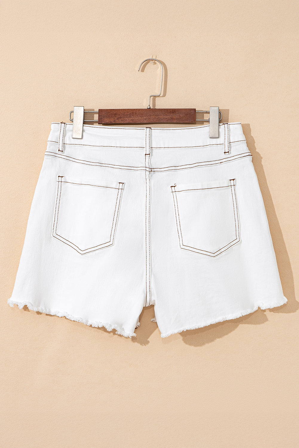 White denim shorts with high waist, frayed raw hem, back patch pockets, belt loops, and button closure.