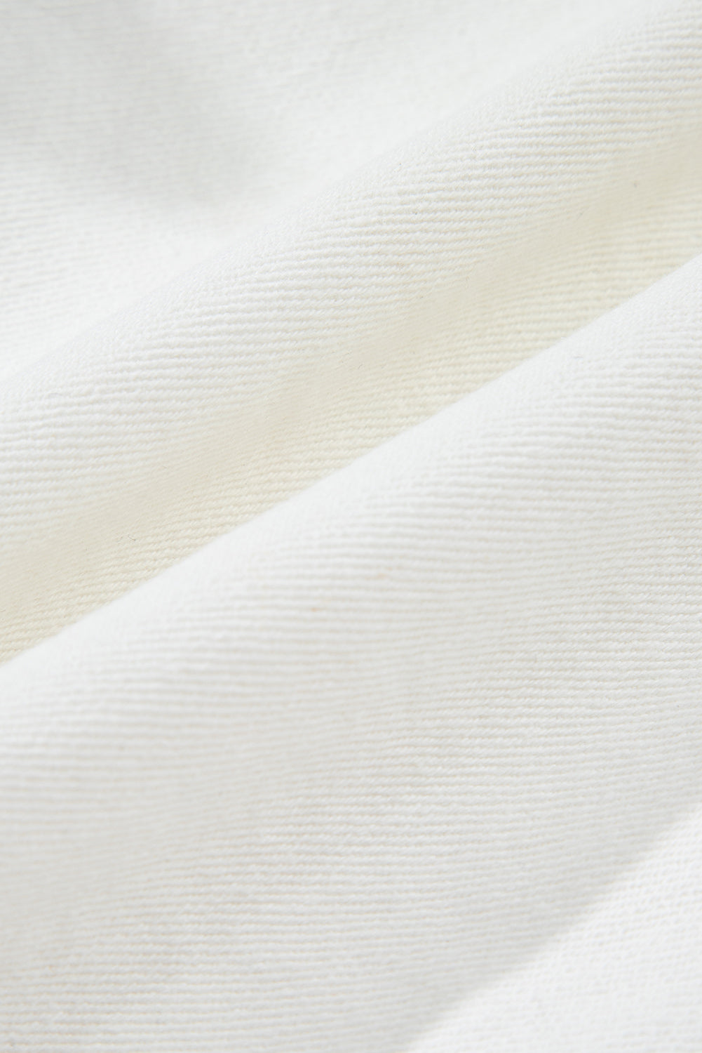 White denim fabric close-up showing fine woven texture and subtle surface grain.