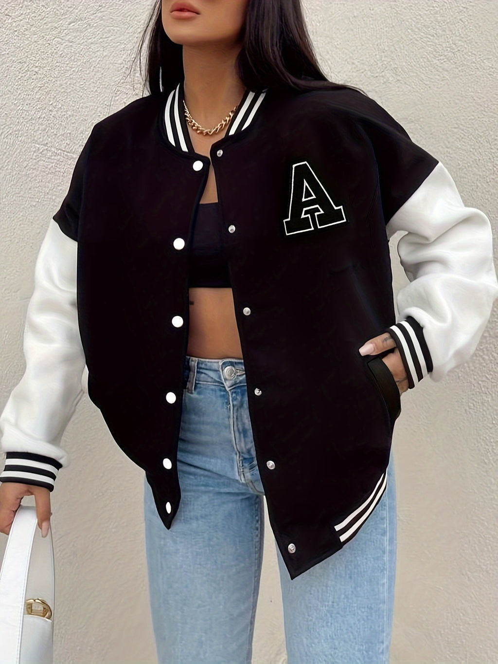 Black varsity bomber jacket with white contrast sleeves, striped cuffs, snap buttons, A logo
